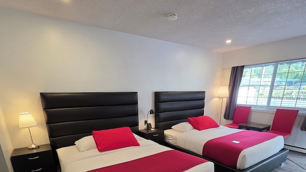 A hotel room with two beds, a nightstand, a lamp, and a window with a view. - Alpine Motel (Hope)