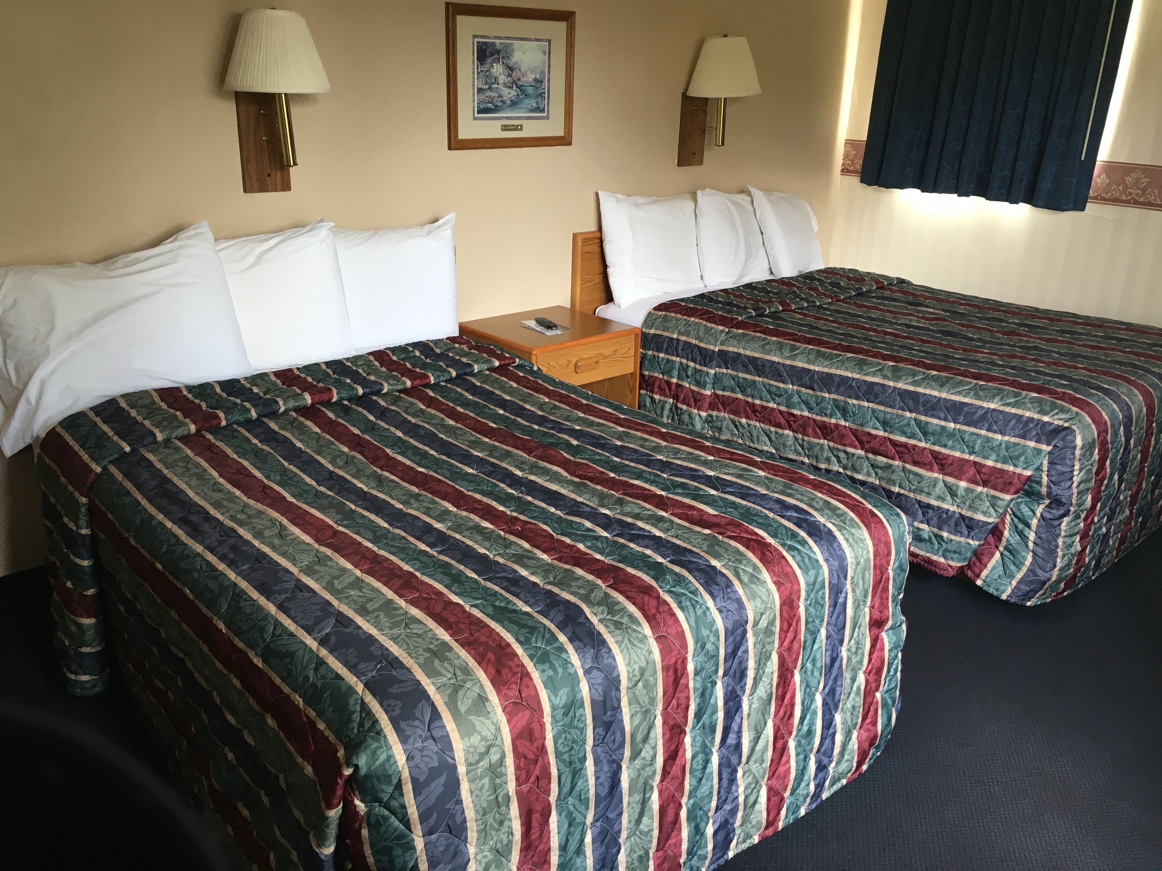 A hotel room with two beds, each with striped bedding, a nightstand, a framed picture on the wall, and two wall-mounted lamps.
