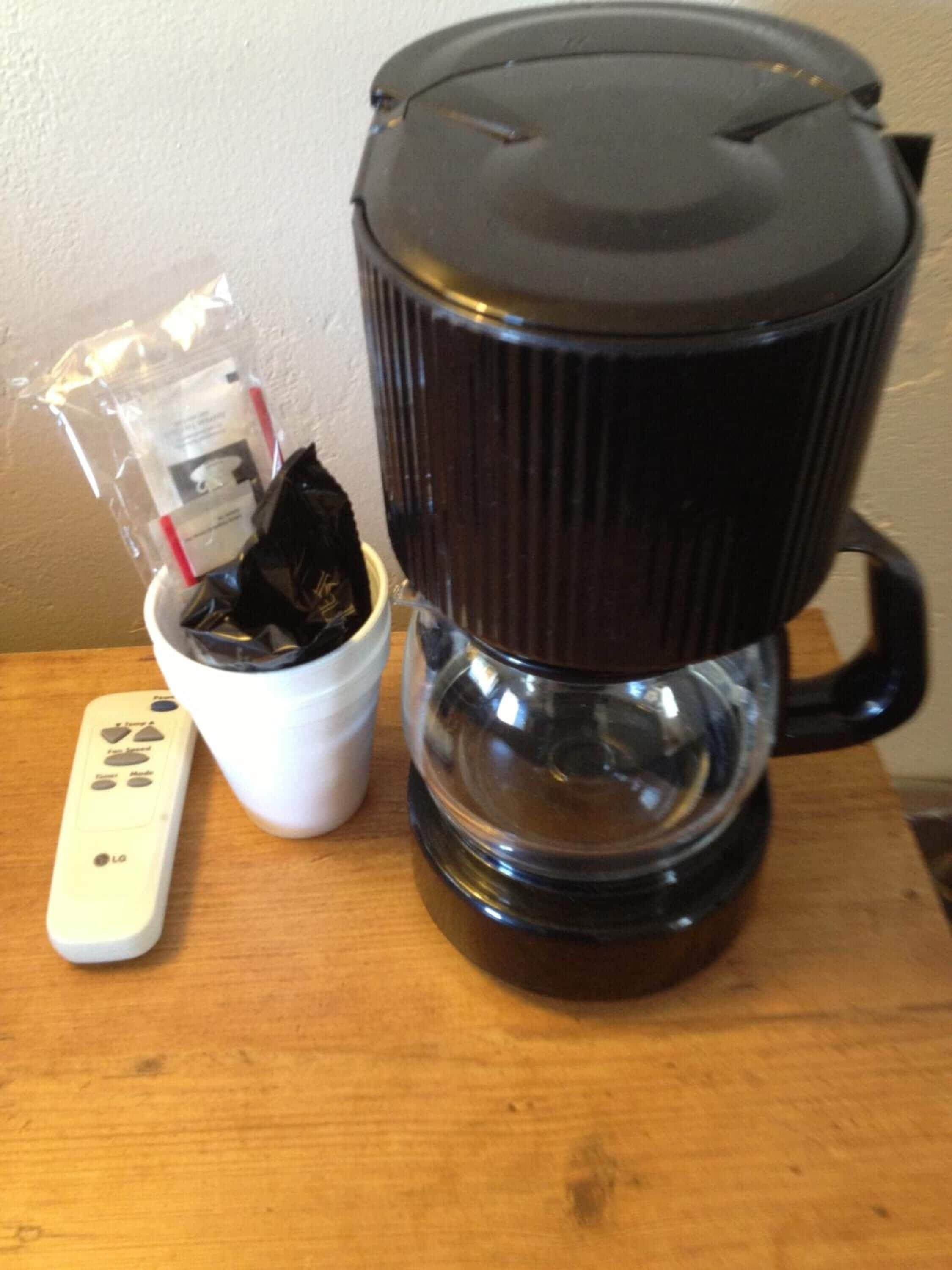 Une machine à café dotée d’une verseuse noire et d’un récipient blanc, avec une télécommande placée à côté.