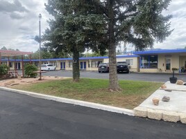 Un motel con techo azul, un estacionamiento y un gran árbol en primer plano.