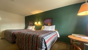 A hotel room with two beds, a small table, and a chair. - The Monticello Inn (Monticello)
