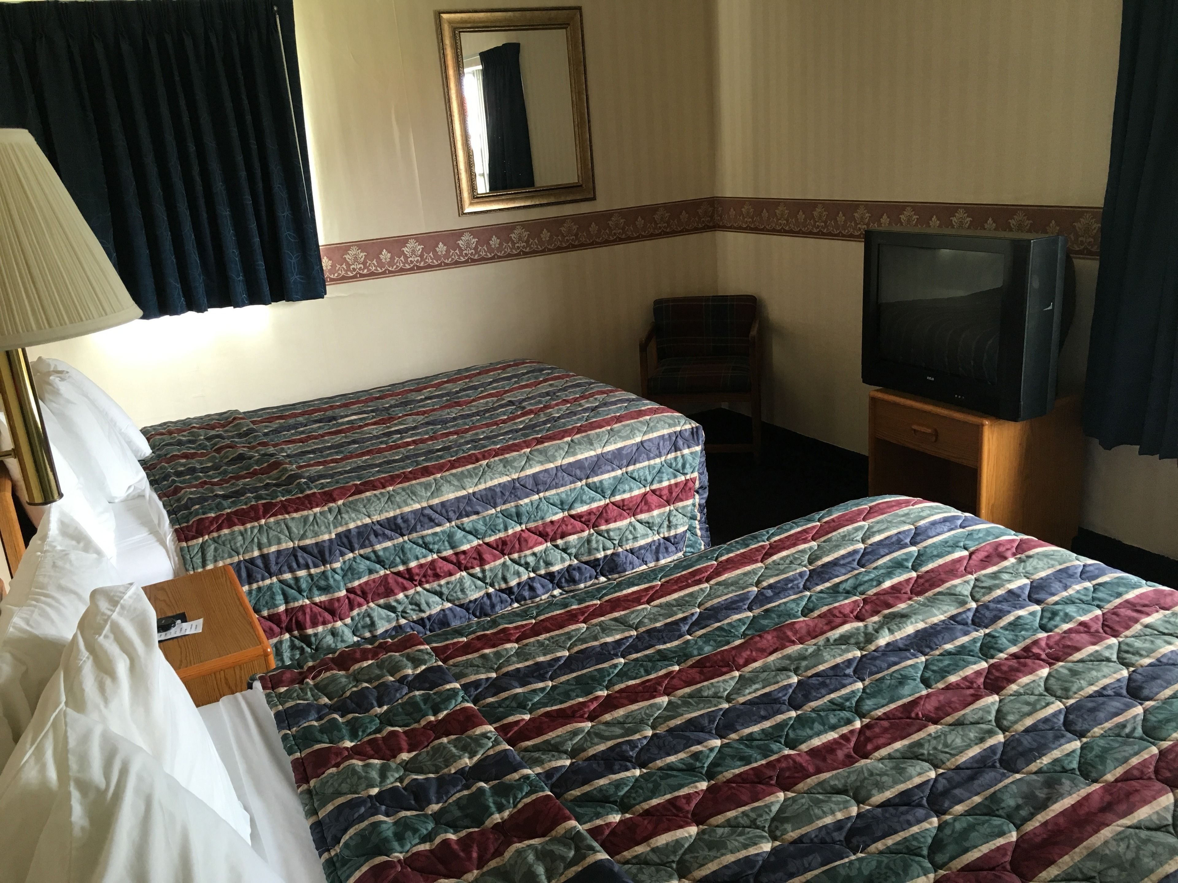 A hotel room with two beds, a TV, a chair, and a lamp.