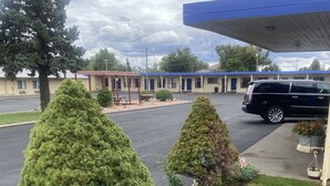 A motel with a parking lot, a covered outdoor seating area, and neatly trimmed trees. - The Monticello Inn (Monticello)