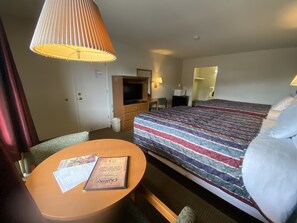 A hotel room with a bed, a television, a desk with a chair, a table, and a lamp.