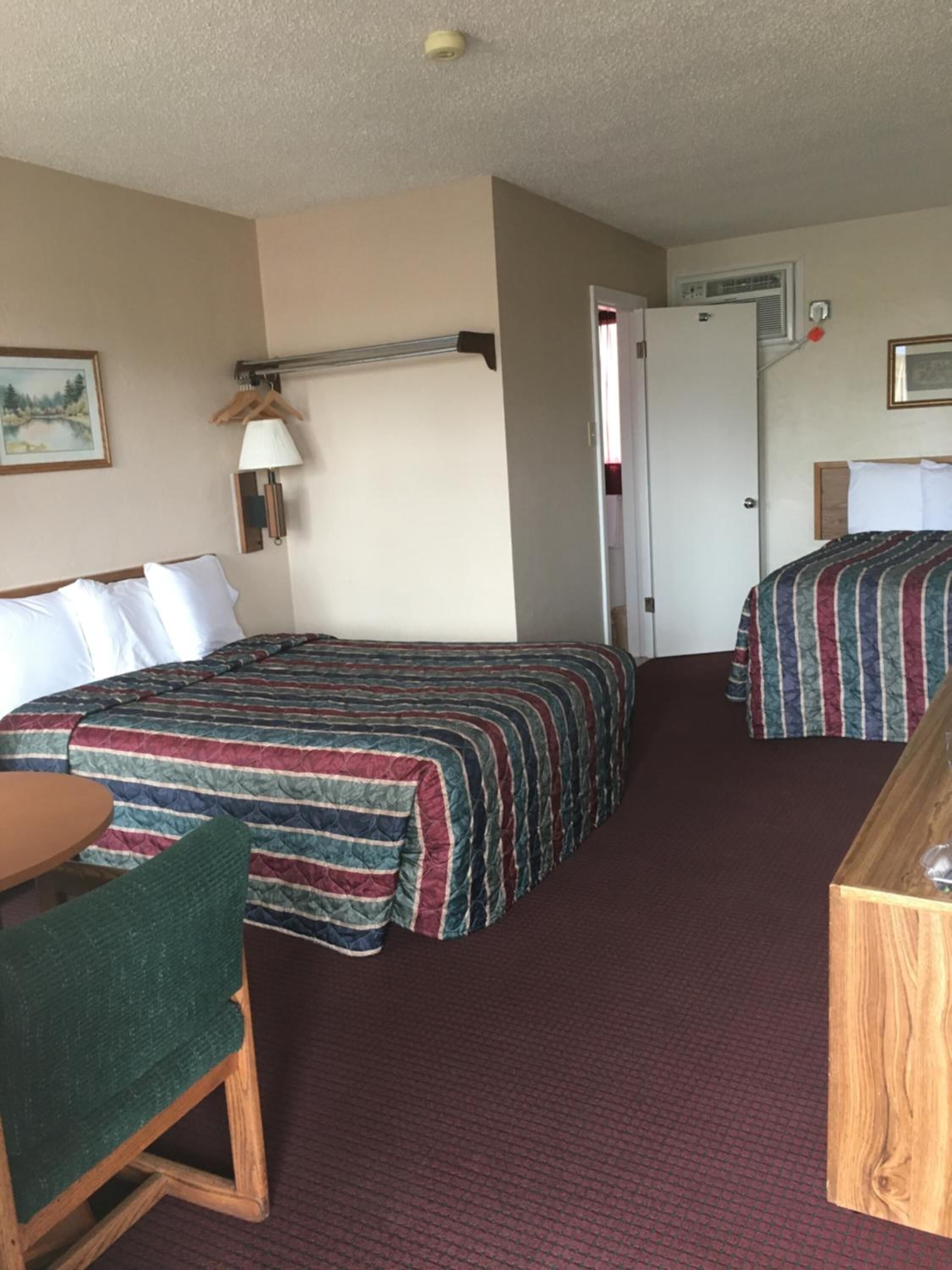 Una habitación de hotel con dos camas, un escritorio, una silla, una lámpara y una puerta.