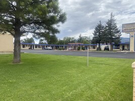 Un motel con techo azul, estacionamiento y un área verde con un árbol.