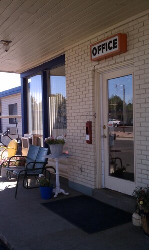 An office building with a sign that reads "OFFICE" above the entrance. There are outdoor chairs and a table with potted plants outside.