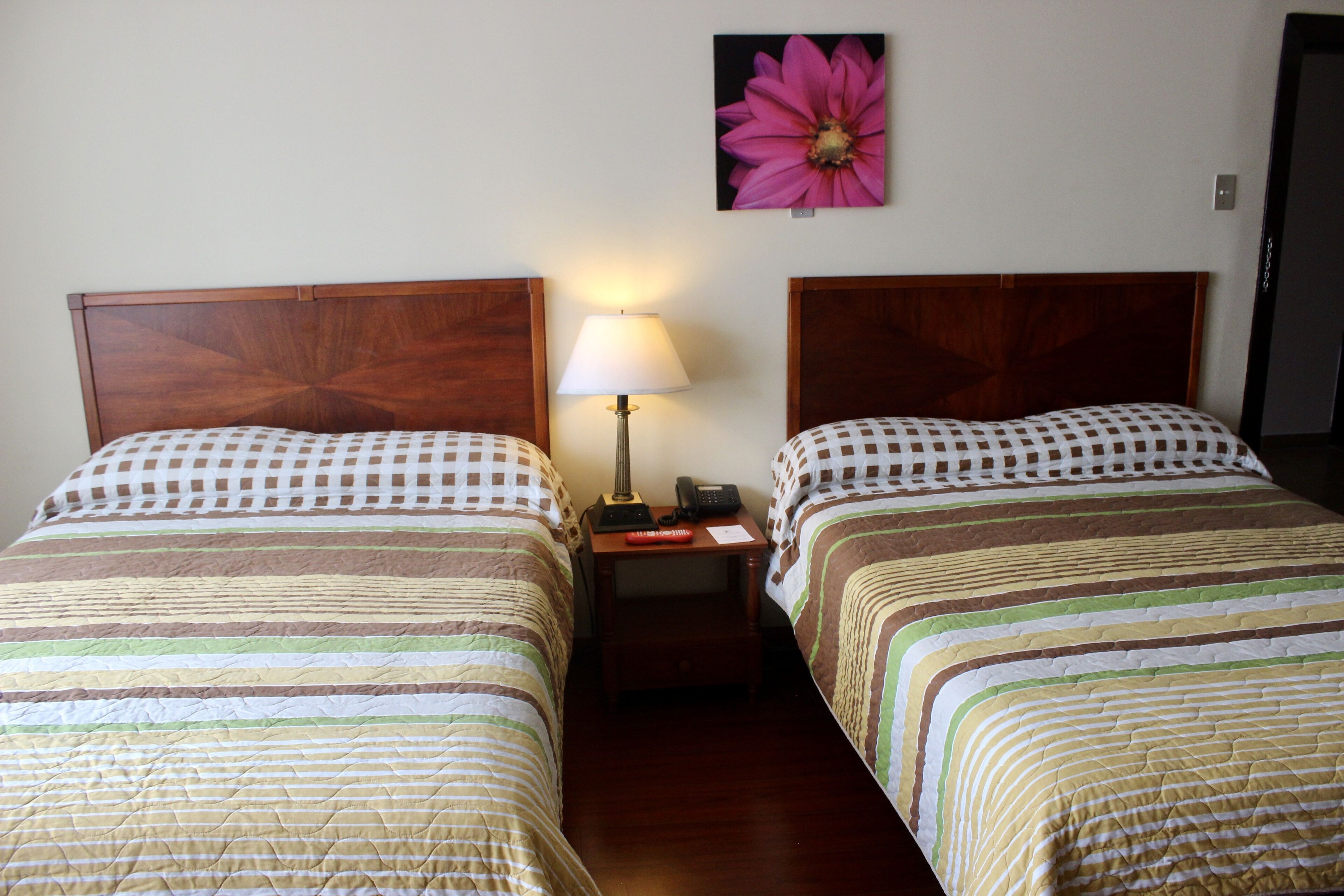 A hotel room with two beds, a nightstand with a lamp, and a wall-mounted flower.