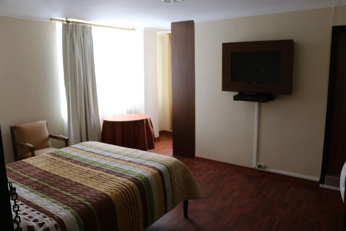 Une chambre d’hôtel avec un lit, une chaise, une petite table, un téléviseur et une porte.
