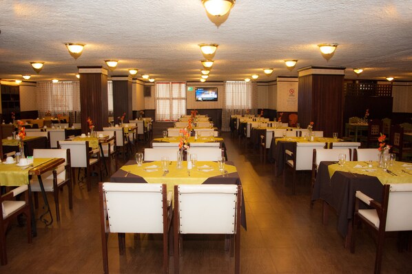 A large dining hall with multiple tables, chairs, and a television screen. - Hotel 6 de Diciembre (Quito)