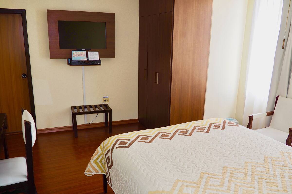Une chambre d’hôtel équipée d’un lit, d’un bureau, d’une chaise, d’une armoire et d’un téléviseur fixé au mur.