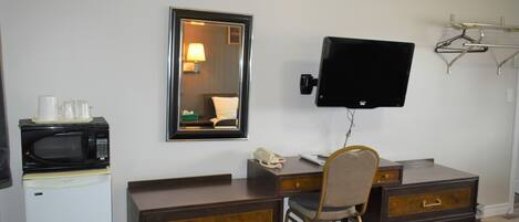 Habitación de hotel con escritorio, silla, televisión, microondas y refrigerador.