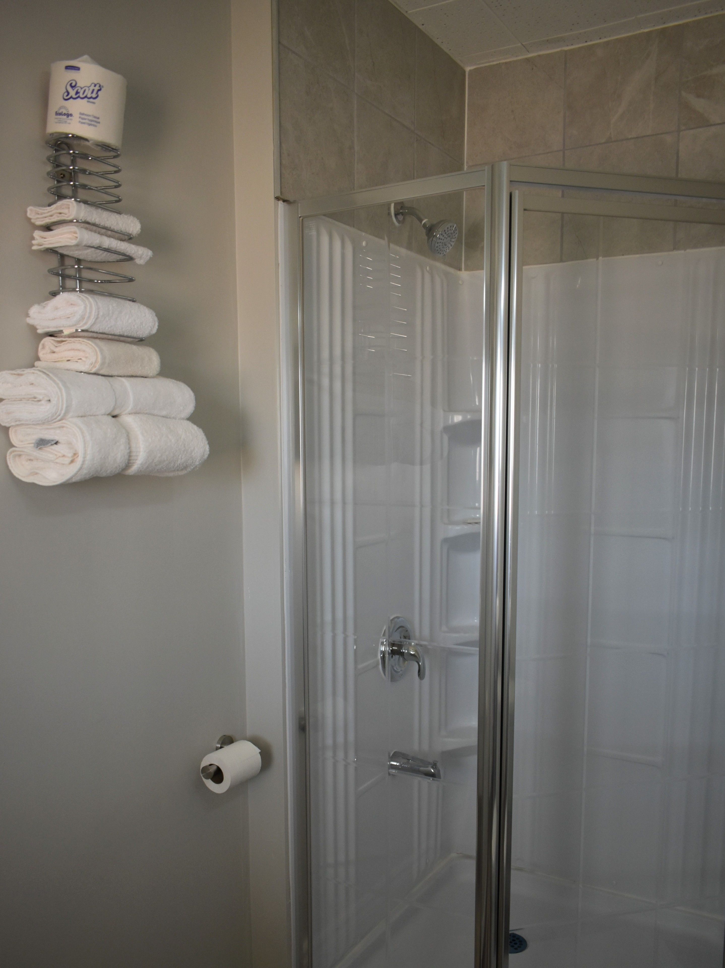 A glass-enclosed shower stall with a towel rack holding several folded towels.
