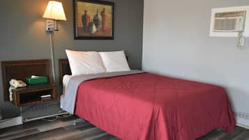 Habitación de hotel con cama, mesita de noche con lámpara, un cuadro en la pared y ventana con unidad de aire acondicionado.