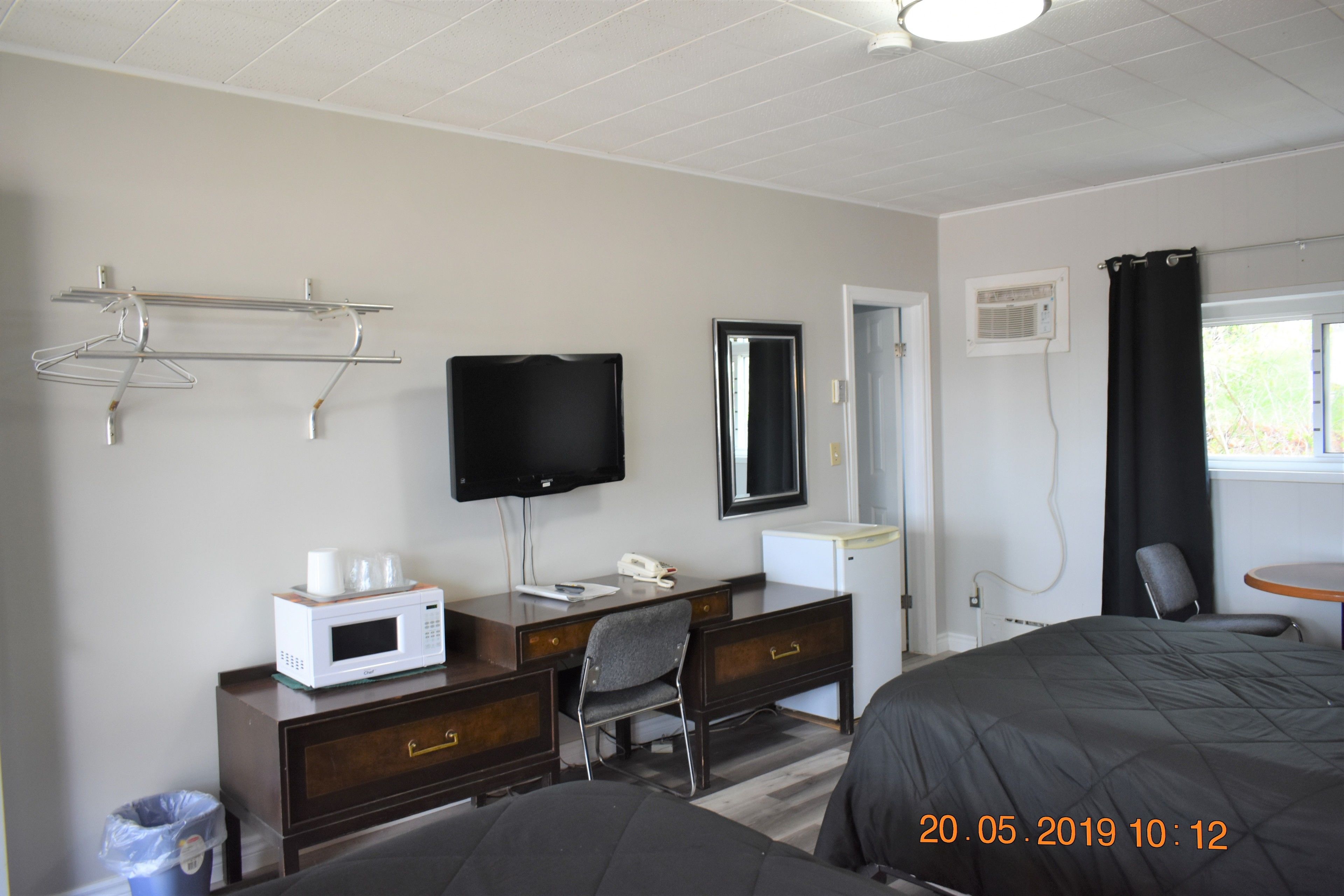 A hotel room with a bed, a desk with a computer, a TV, and a window with curtains.