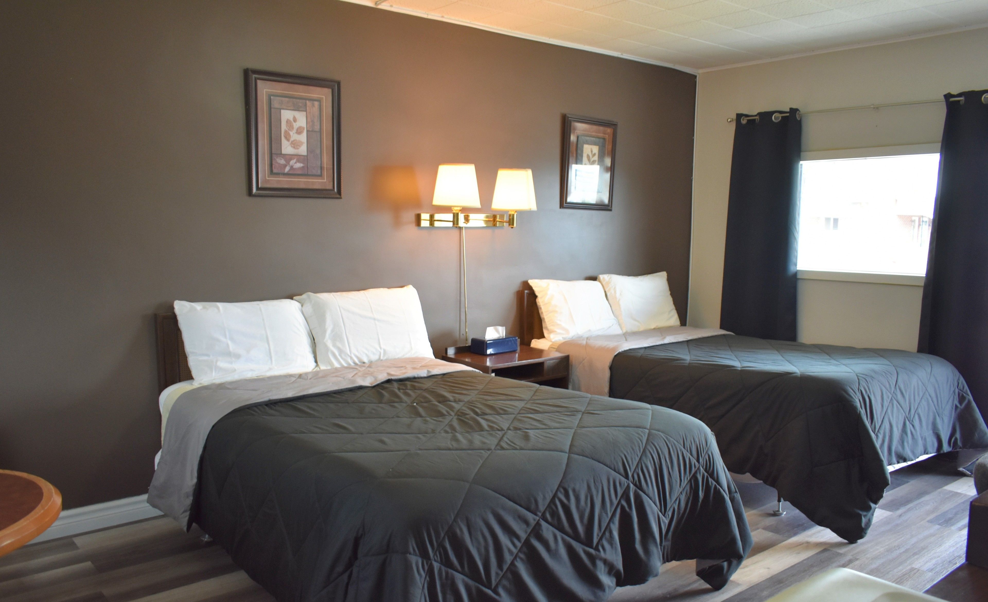 A hotel room with two beds, a nightstand, a lamp, and a window with curtains.