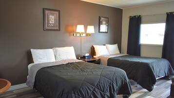A hotel room with two beds, a nightstand, a lamp, and a window with curtains.