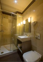 Un baño moderno con ducha envuelta en vidrio, un lavamanos con espejo y un inodoro.