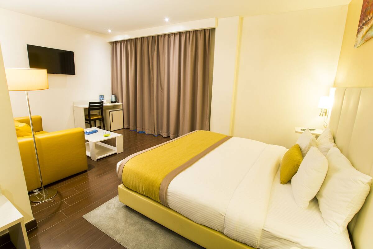 A hotel room with a bed, a desk, a chair, a TV, and a window with curtains.