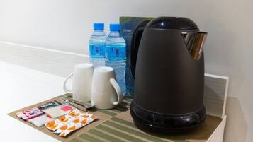Habitación de hotel con cafetera, dos botellas de agua, una taza blanca, un hervidor blanco y una pequeña mesa con artículos de aseo.