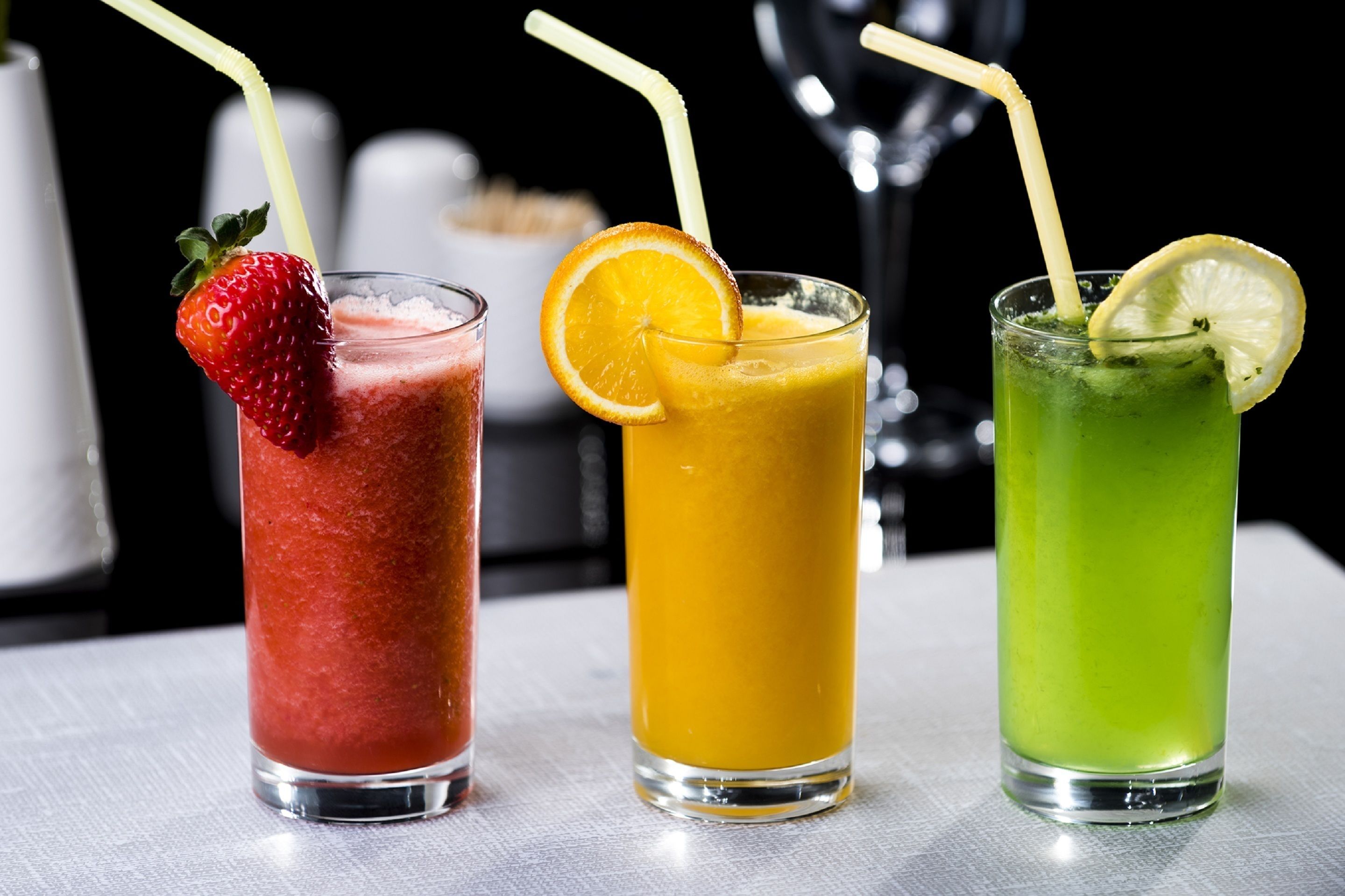 Tres vasos de bebidas de colores distintos, cada uno con una pajita y una rodaja de fruta como adorno.