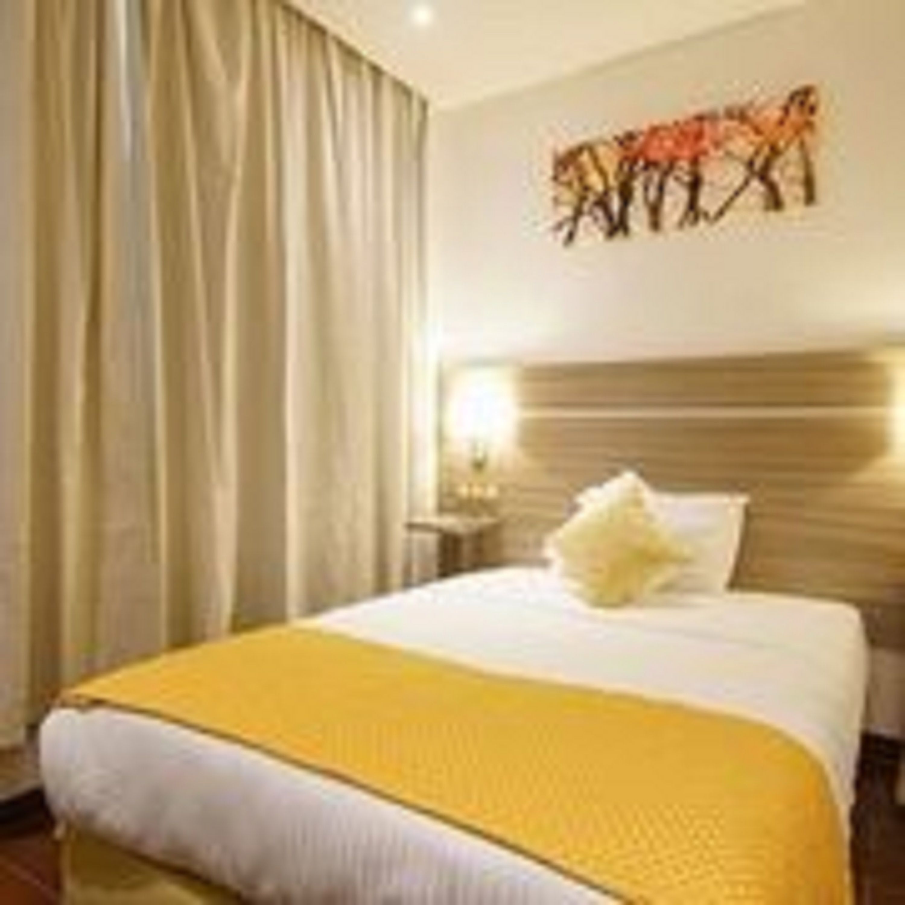 Quarto de hotel com cama, cortinas, mesa de cabeceira e uma obra de arte na parede.
