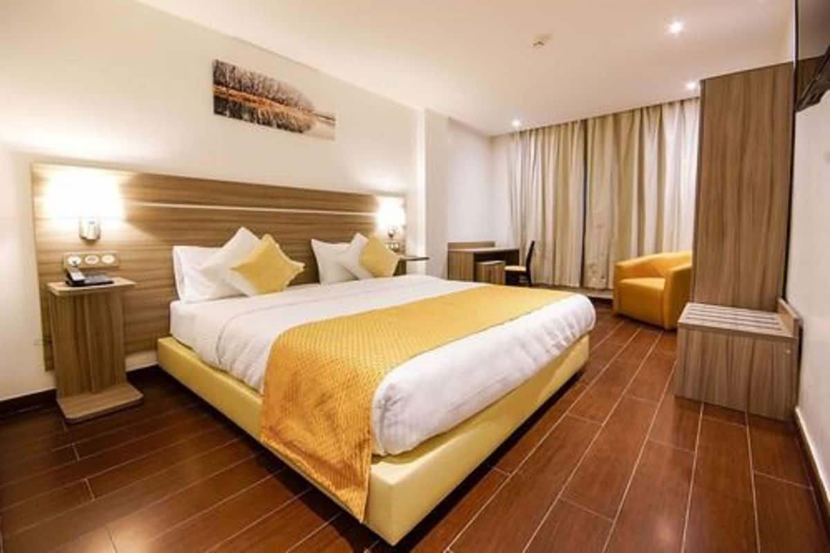A hotel room with a large bed, a bedside table, a chair, and a window with curtains.