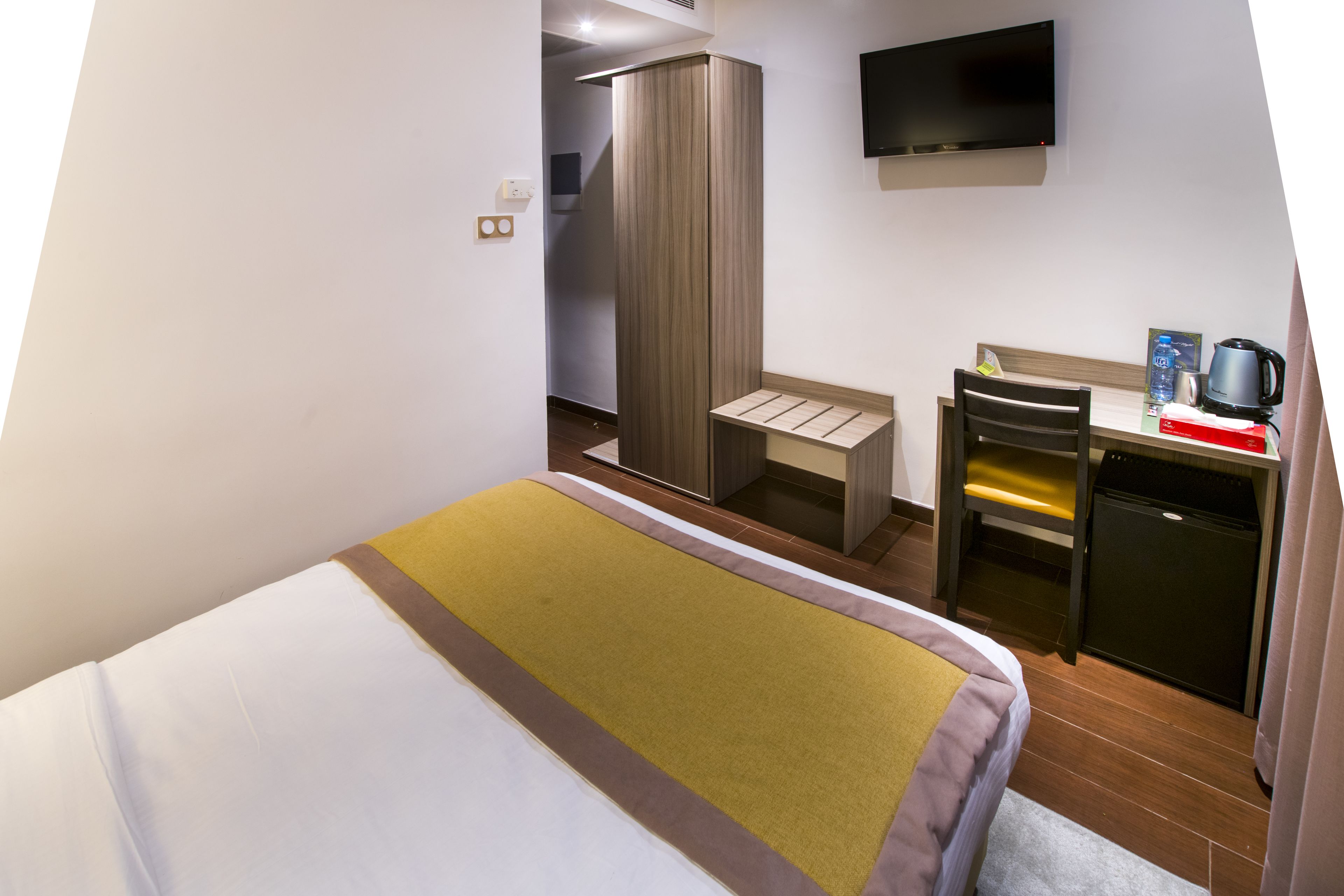 A hotel room with a bed, a desk, a chair, a wardrobe, a television, and a coffee machine.