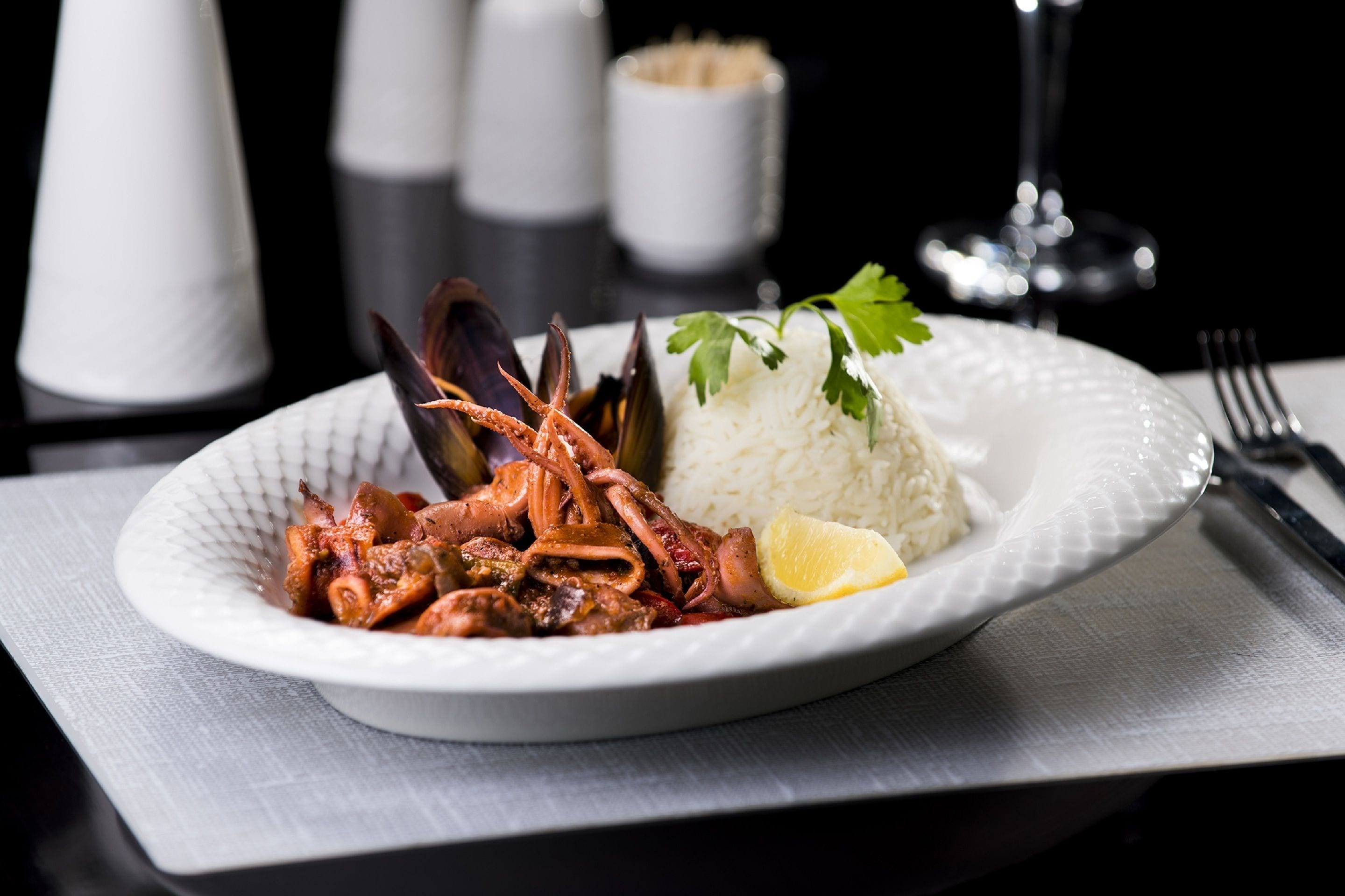 A plate of seafood with rice and lemon on a white plate.