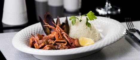 A plate of seafood with rice and lemon on a white plate.