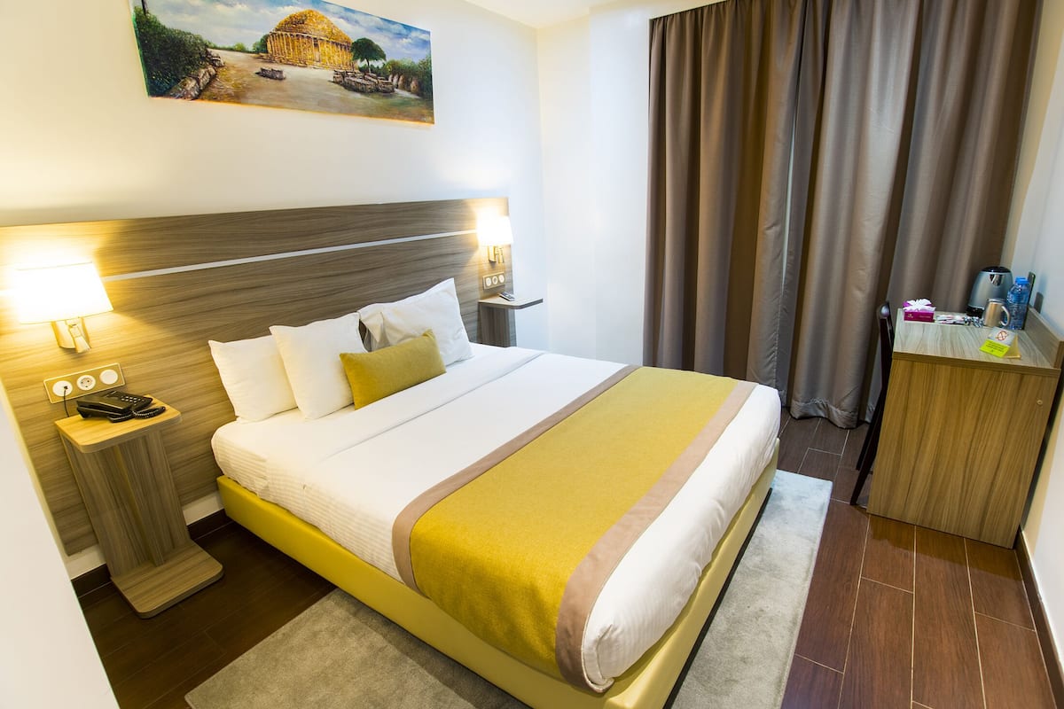 A hotel room with a bed, bedside tables, a desk, a chair, a painting on the wall, and a curtain.
