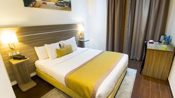 A hotel room with a bed, bedside tables, a desk, a chair, a painting on the wall, and a curtain.