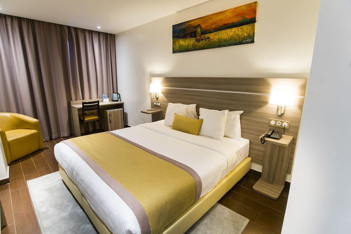A hotel room with a large bed, a desk, a chair, and a painting on the wall.