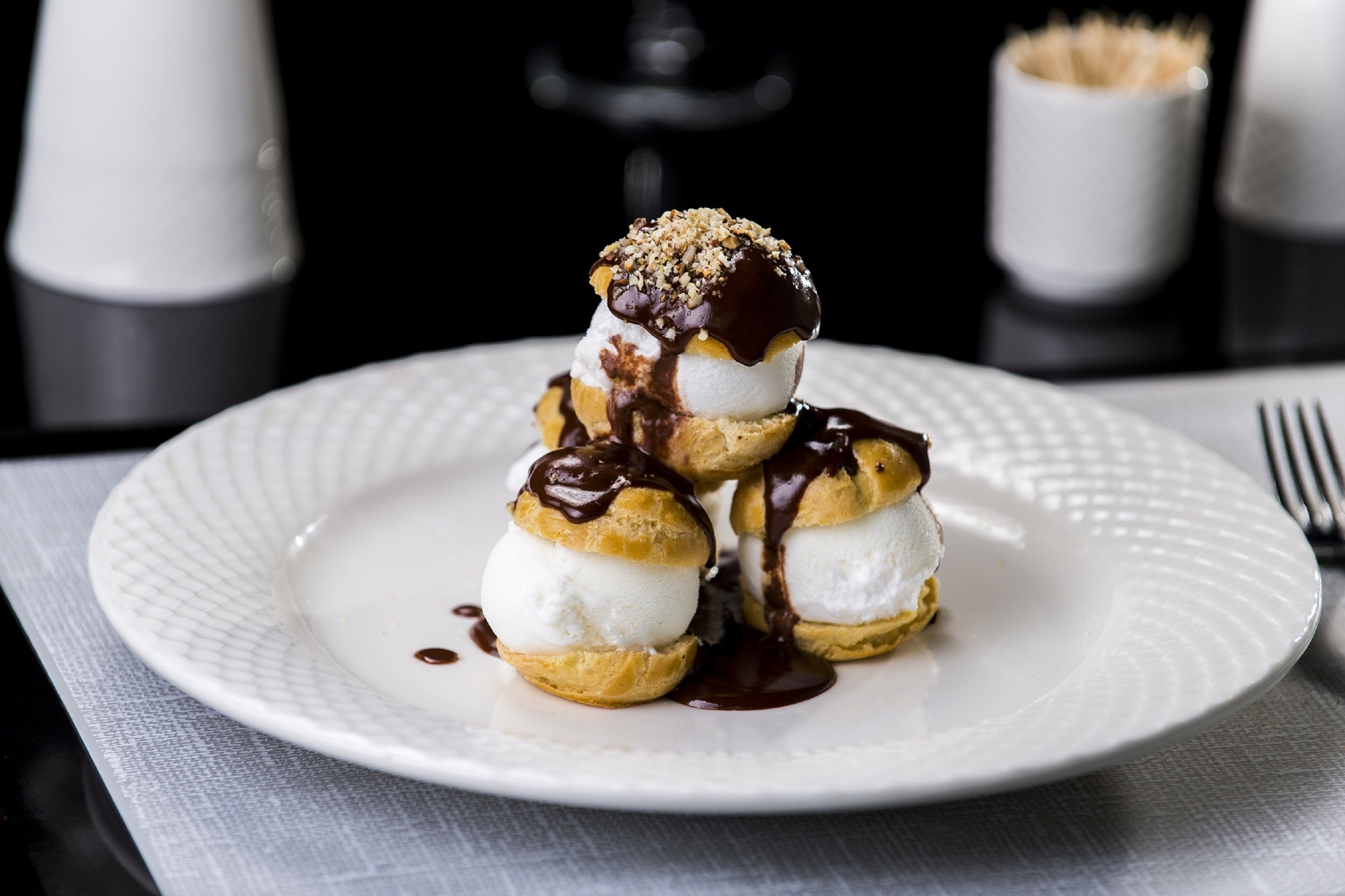 A plate of profiteroles with chocolate sauce and nuts on a white plate.