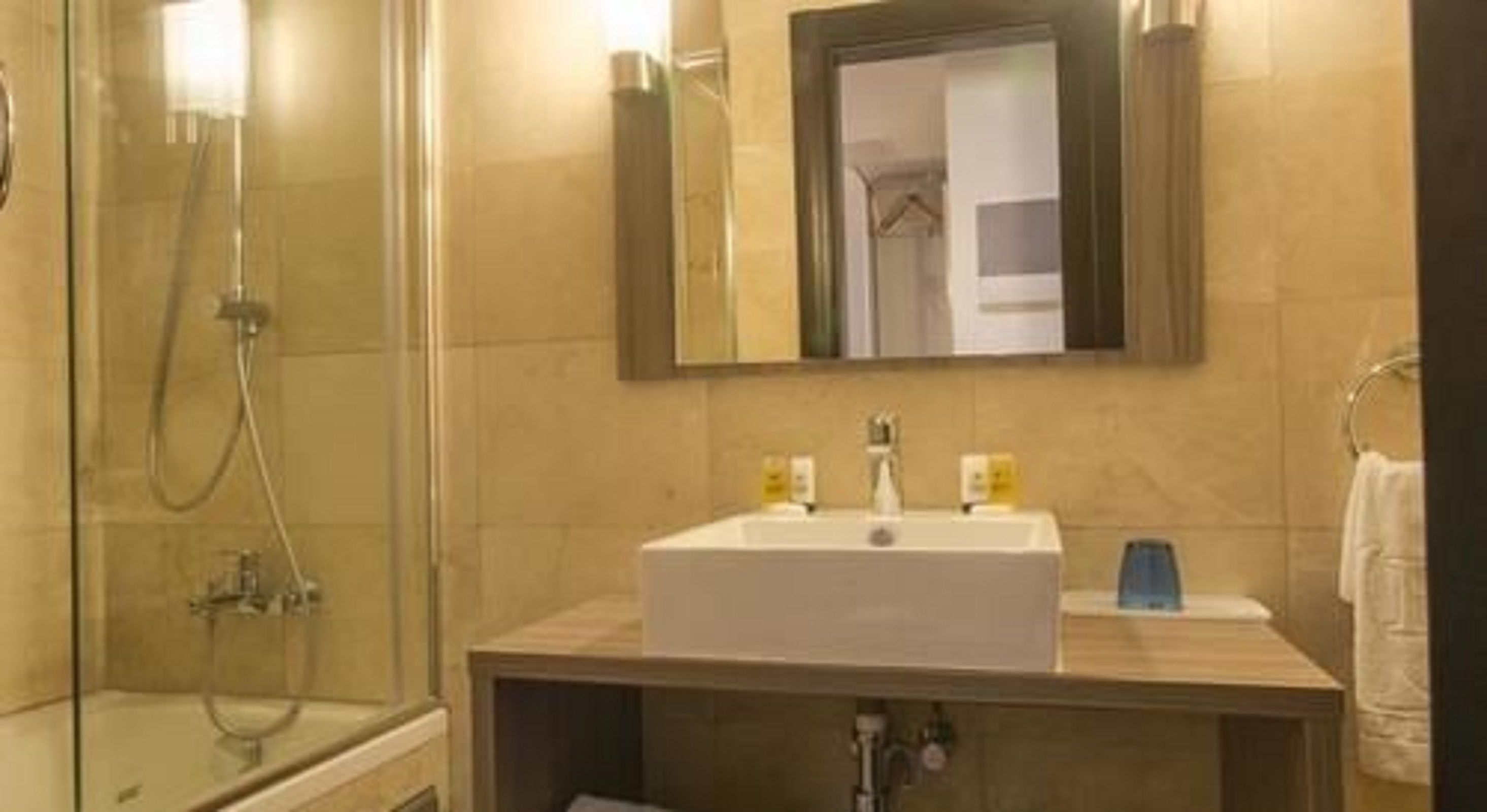 Un baño con ducha de vidrio, un lavamanos blanco con un espejo encima y un perchero a la derecha.