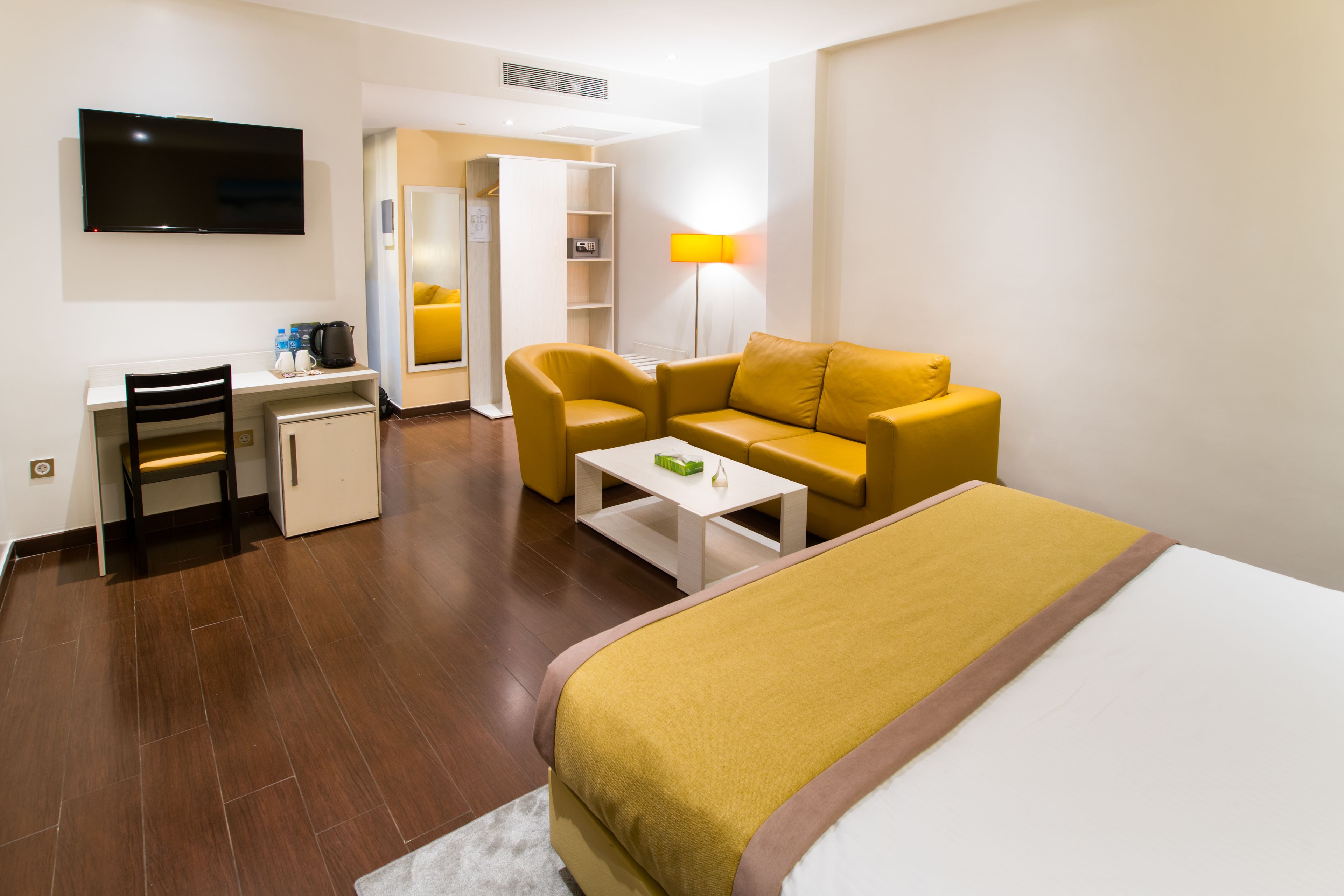 Una camera d'albergo con un letto, una scrivania, una sedia, un divano, una televisione e una lampada.