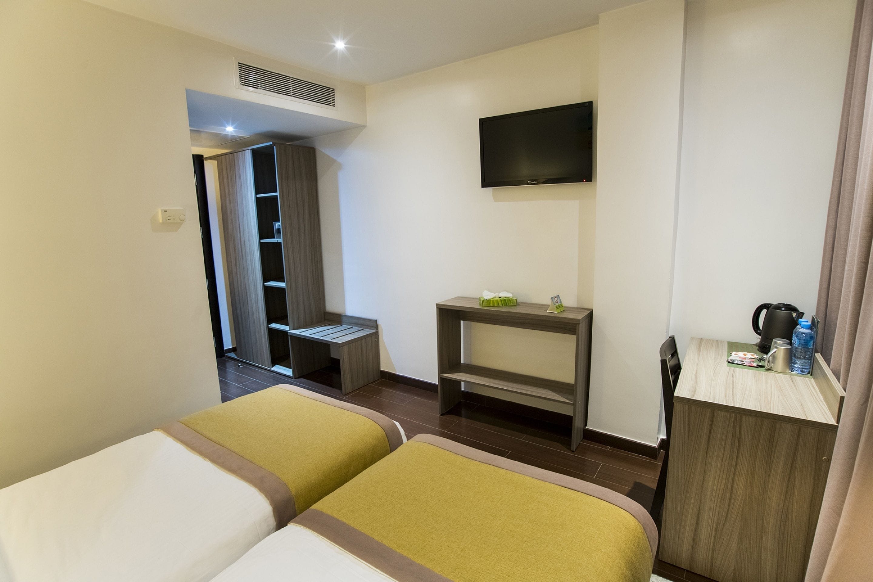 A hotel room with two beds, a TV, a small desk with a kettle, and a wardrobe.