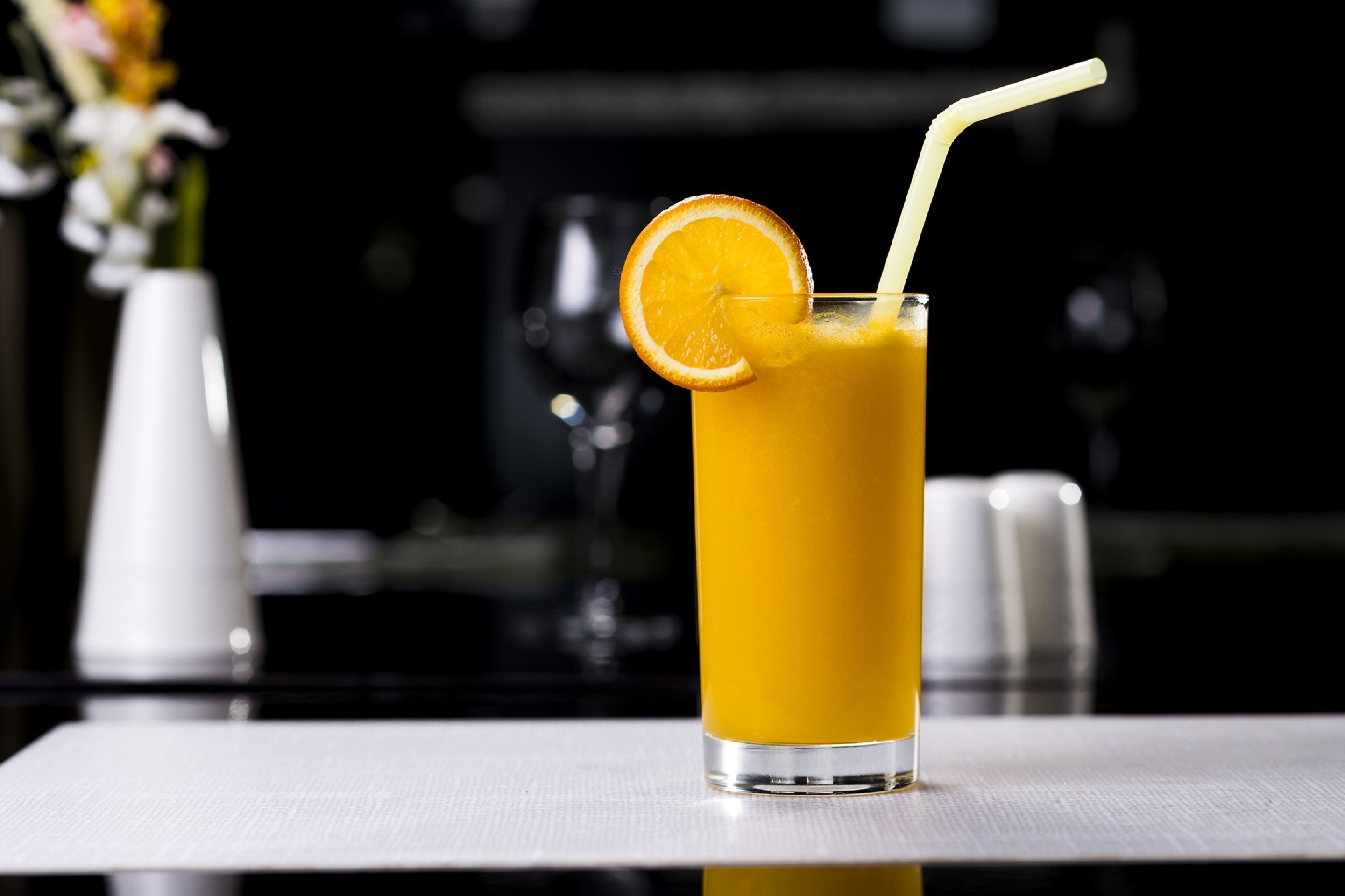 A tall glass of orange juice with a straw and an orange slice garnish on a white table.