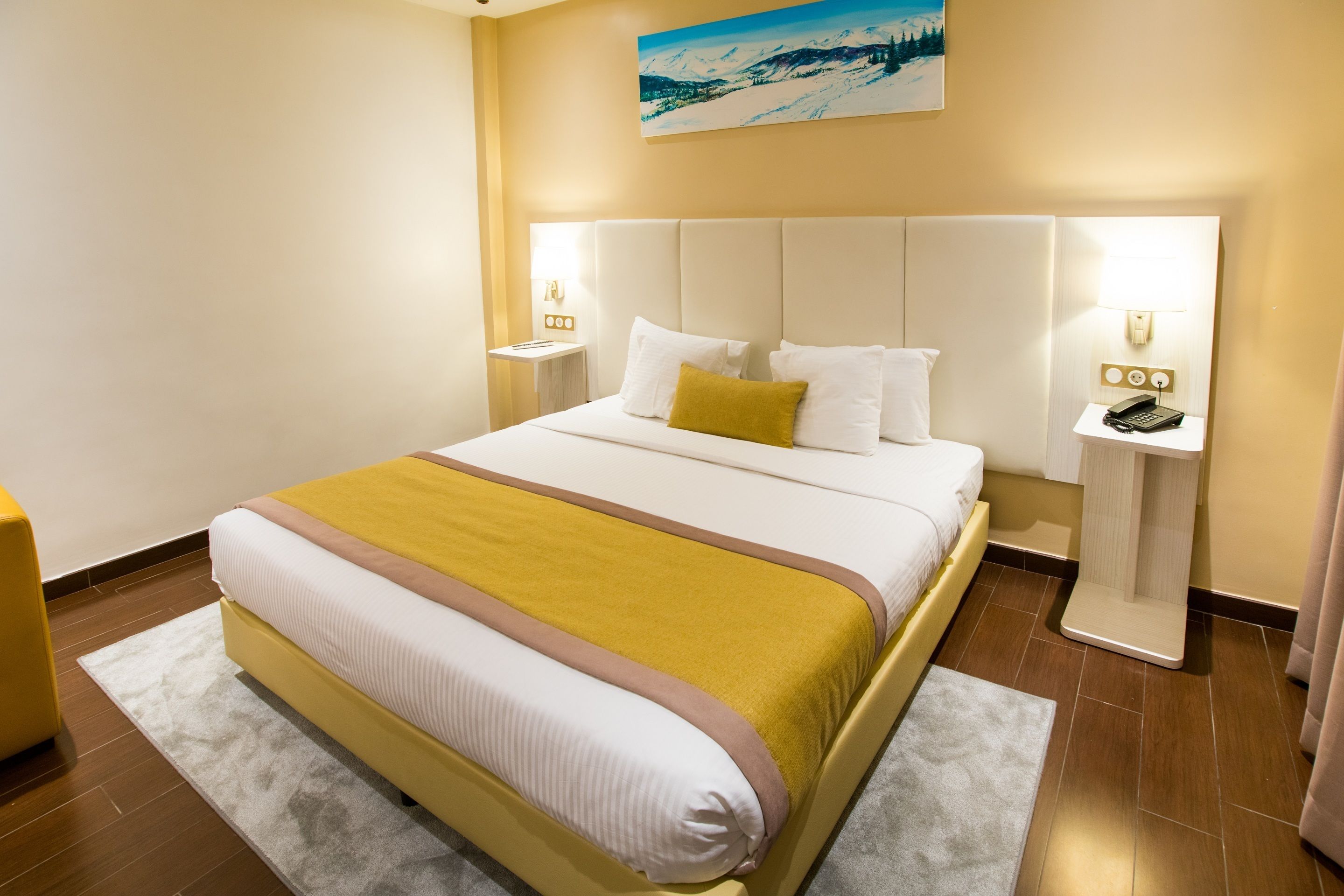A hotel room with a large bed, a bedside table with a lamp, and a painting on the wall.