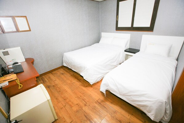 A hotel room with two single beds, a desk with a computer and telephone, and a small refrigerator.