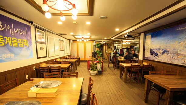 A restaurant interior with wooden tables and chairs, a large poster on the wall, and a ceiling light fixture. - Goodstay Daegwallyeongsanbang (Pyeongchang)