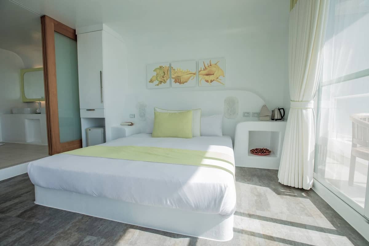 A modern hotel room with a large bed, a bedside table, a nightstand, a mirror, and artwork on the wall.