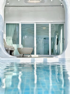 Un área de piscina moderna con puertas de vidrio transparente, una silla de descanso y una mesita.