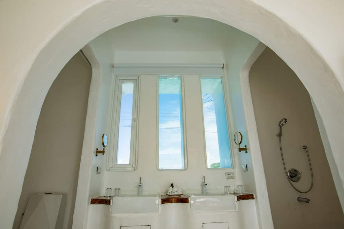 A bathroom with an arched ceiling, three windows, a shower, and a sink with a mirror.