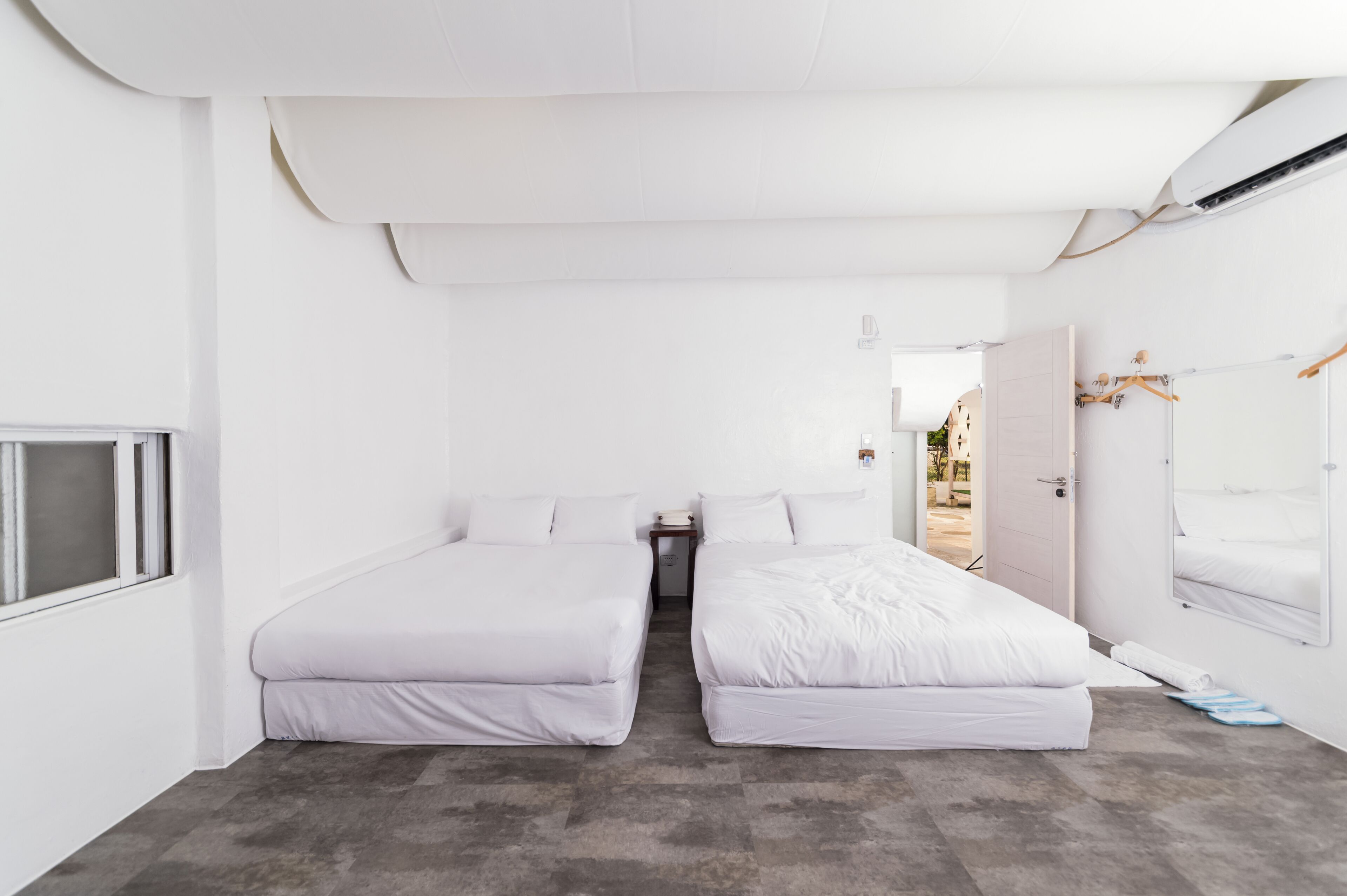 Una habitación con dos camas, una mesita, un espejo y una ventana.