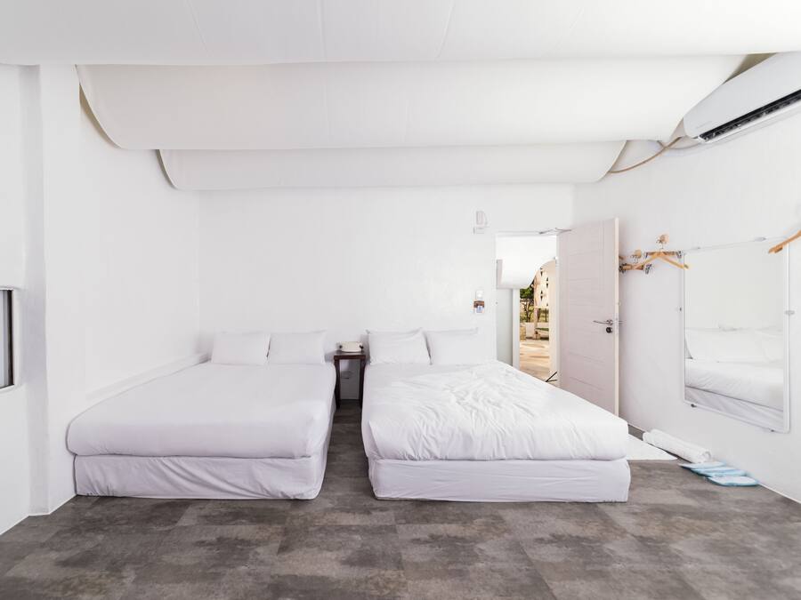 Una habitación con dos camas, una mesita, un espejo y una ventana.