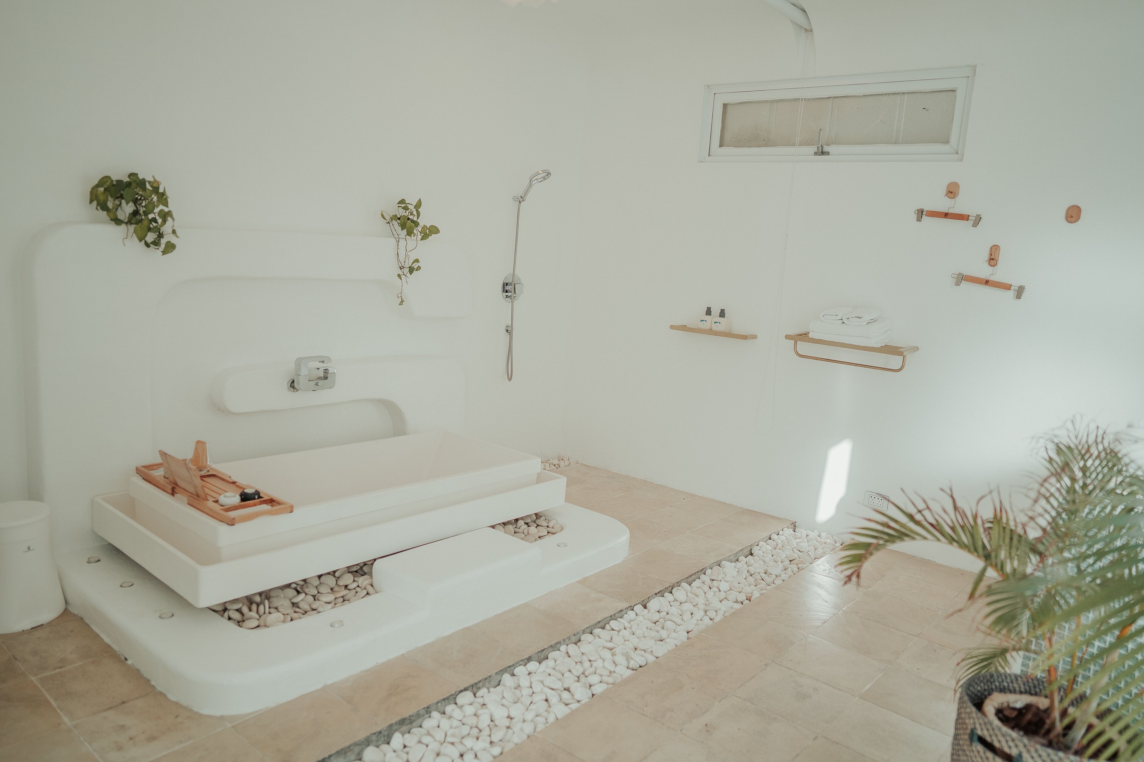 Un baño moderno con una bañera grande, una ducha y un lavamanos pequeño. Hay plantas y un perchero en las paredes.
