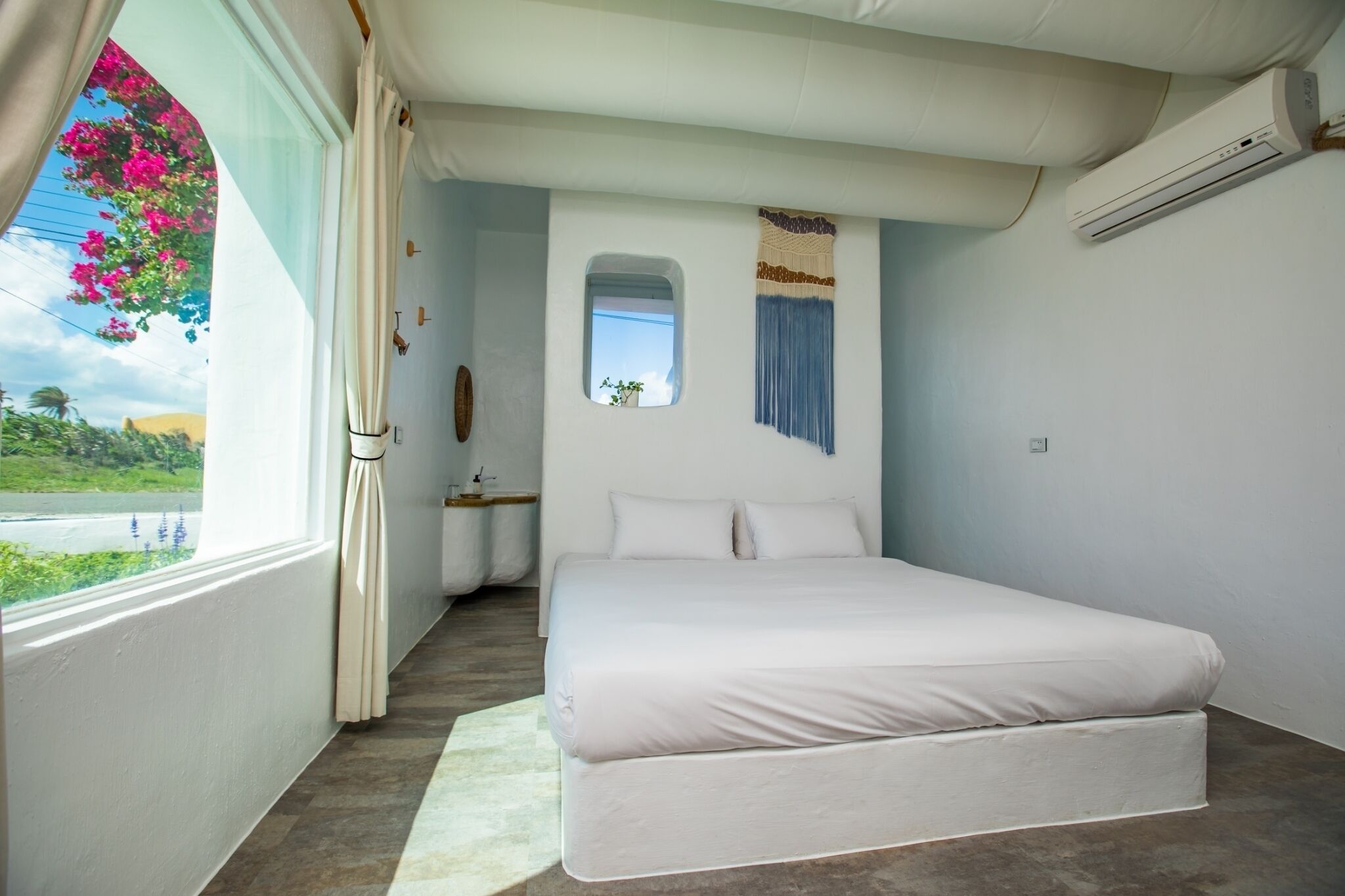 A bedroom with a large bed, a window with curtains, a small window, and an air conditioning unit.