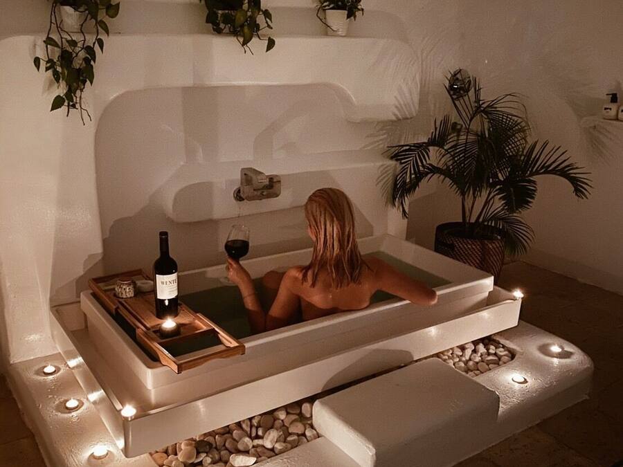 A spa tub with a bottle of wine and candles, surrounded by plants and a pebble-lined area.