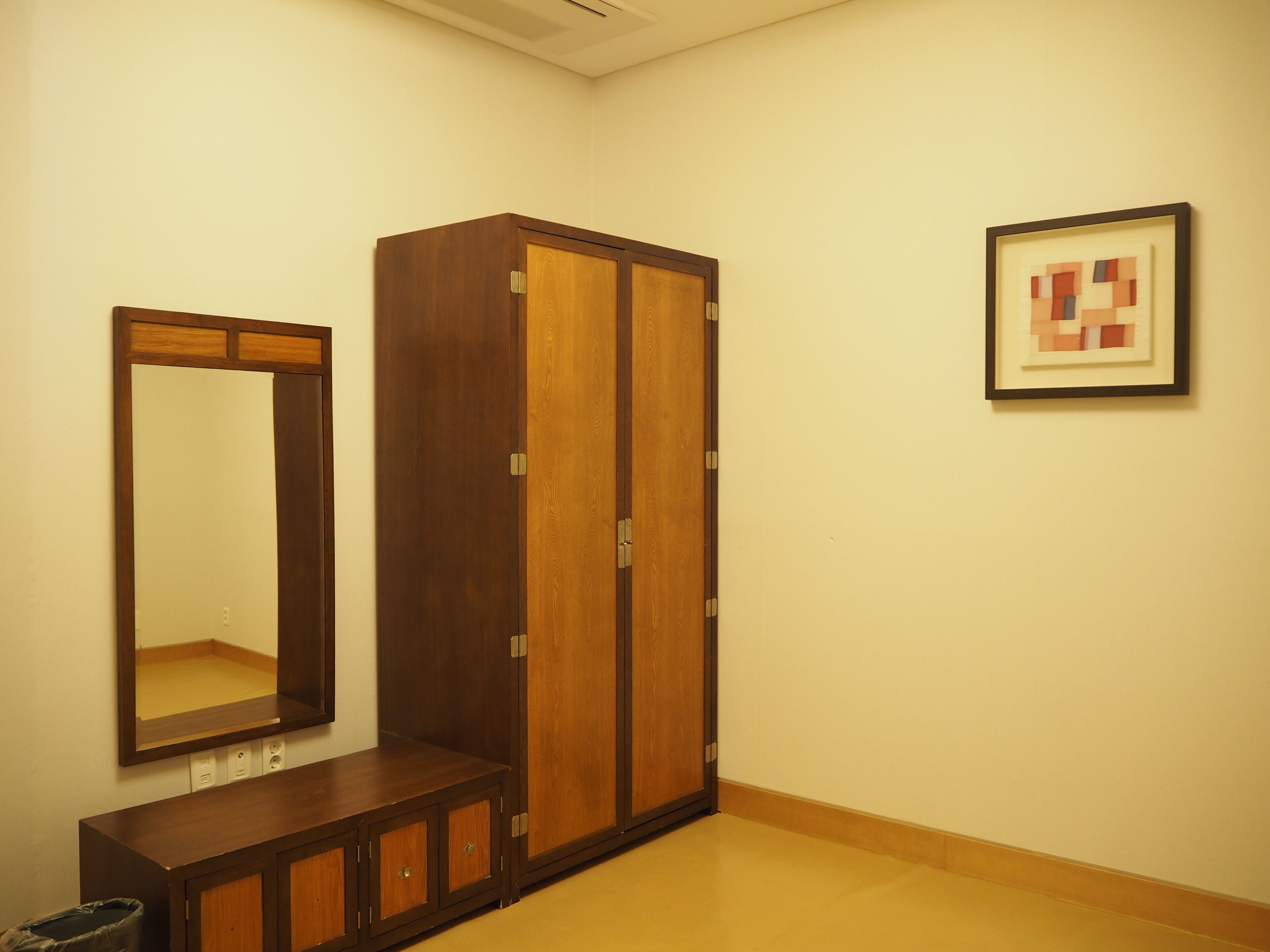 Ein Zimmer mit Holzschrank, Spiegel und einem gerahmten abstrakten Kunstwerk an der Wand.